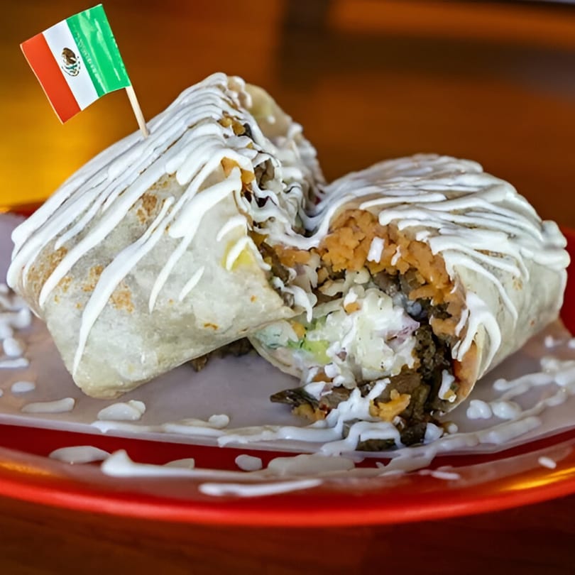 A large burrito, cut in half, drizzled with white sauce, and a Mexican flag toothpick.