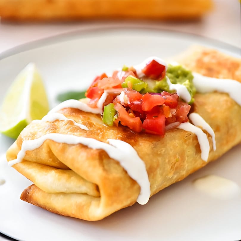 Golden-brown chimichanga topped with pico de gallo, guacamole, sour cream, and a lime wedge.