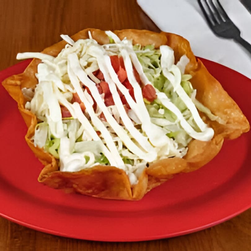 A Taco Station taco salad in a crispy shell, topped with lettuce, tomatoes, and sour cream.