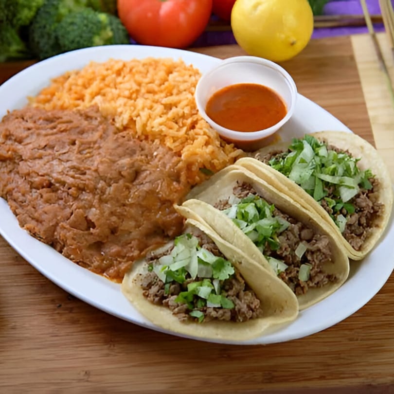 Three beef tacos with lettuce and onions, served with rice, refried beans, and salsa.