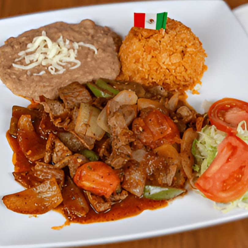 A Mexican dish with steak, rice, refried beans, and a small Mexican flag on a white plate.