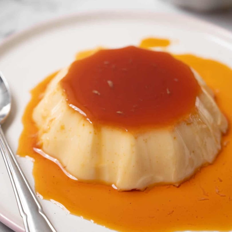 A creamy flan dessert with rich caramel sauce on a white plate, ready to be enjoyed.