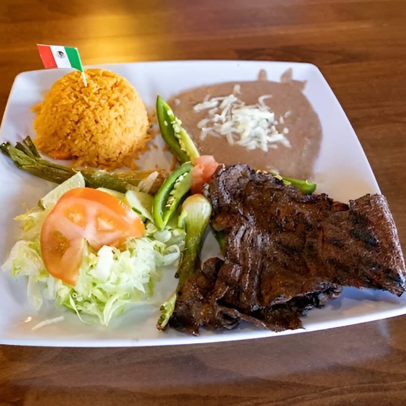 Mexican carne asada plate with rice, refried beans, salad, and a small Mexican flag.